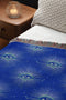 Woven cotton throw blanket with a deep blue background featuring a repeated pattern of all-seeing eyes in gold and seafoam green. The blanket has a colorful fringed edge.